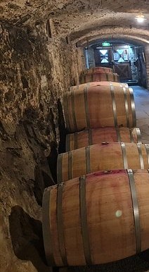 Wine barrels stacked along the wall of a stone underground cellar
